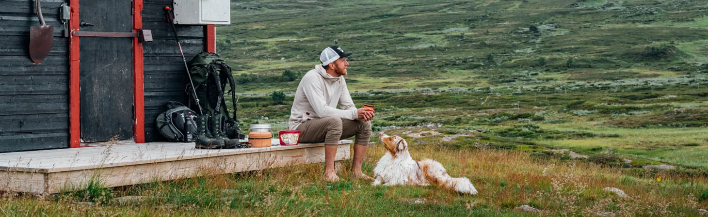 En man och en hund tar en vilopaus ifrån vandringen på fjället