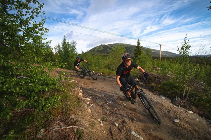 Två personer cyklar mountainbike utför på grävd cykelled.