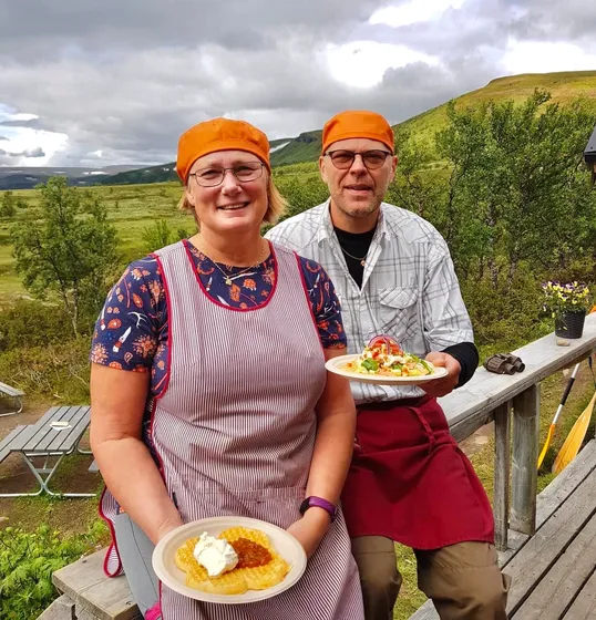 Johan och Marianne håller i tallrikar med våfflor, fjäll i bakgrunden.