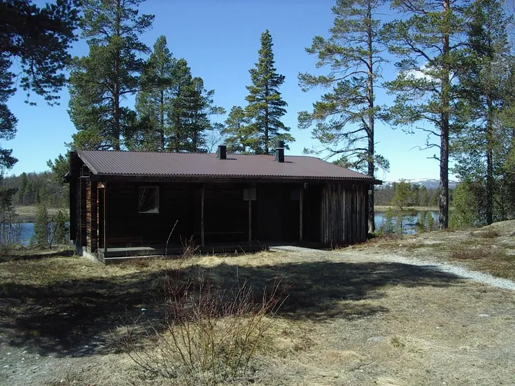 Stuga i skog, vid sjö.